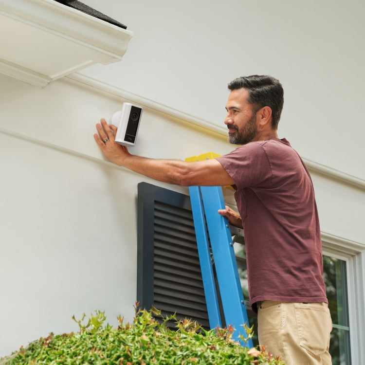 Man on a ladder mounting a white Spotlight Cam Pro (newest gen) onto the side of his home.