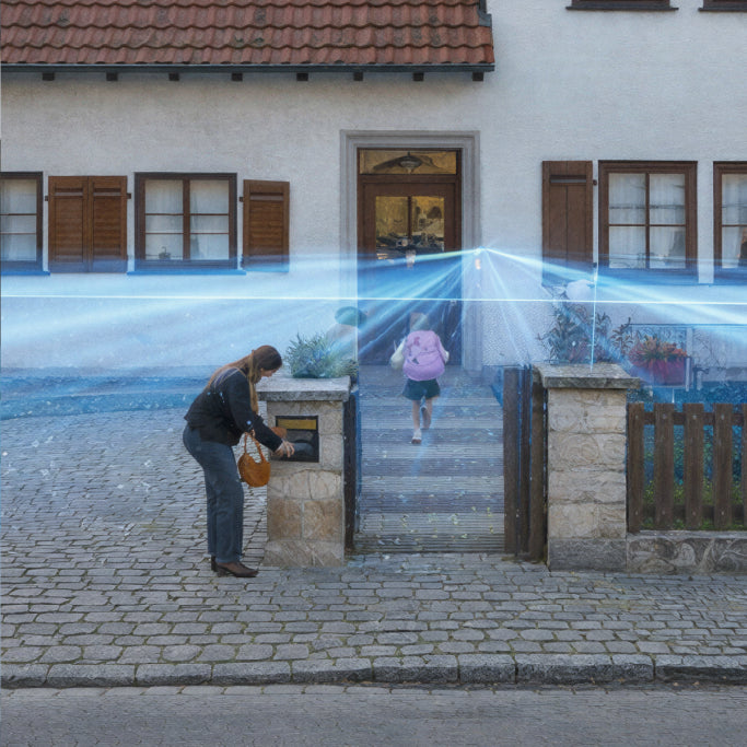 A mother at the letter box of her house while the daughter is walking towards the front door. Light beams from the Battery Video Doorbell Pro demonstrate the zone for motion detection.